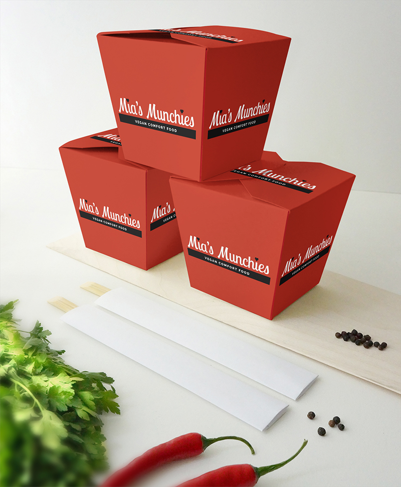 Photograph of three stacked takeout containers with black and white logos on red boxes; light gray background with cilantro, two red hot peppers, black peppercorns, two sets of chopsticks.