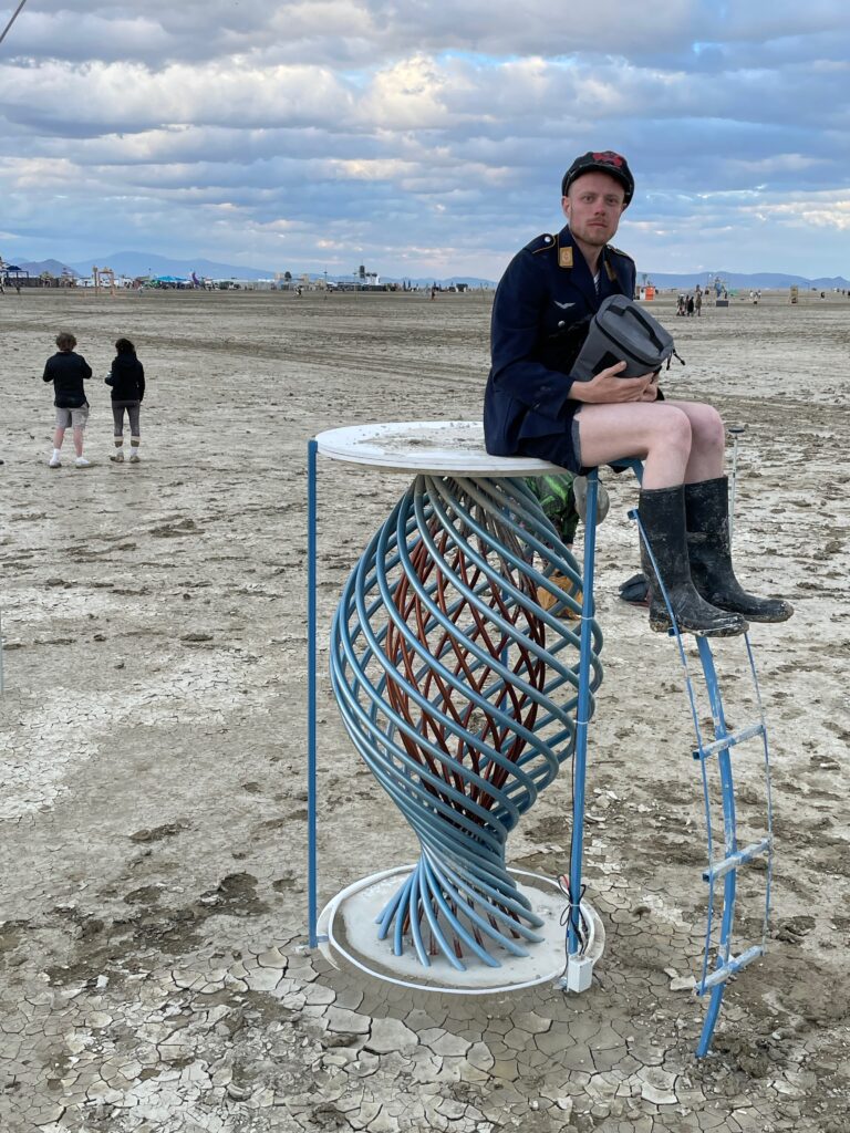 One of my FLG crew, Max, sitting on a 6' high structure of turquoise-colored helical steel rods with a wooden top.