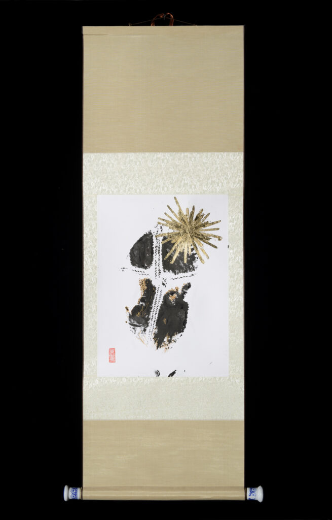 Evoco performance/artwork #4: pale cream brocade fabric scroll with paper mounted on it. Paper has paint impression of a person's back quartered by rope. A starburst has been added in gold leaf.