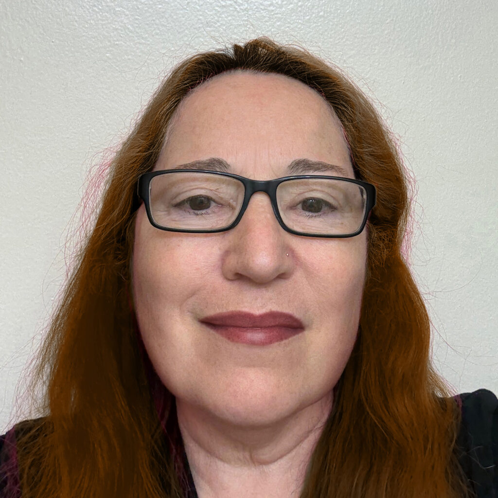 Woman with black-rimmed glasses, auburn hair and black top, smiling at the viewer.