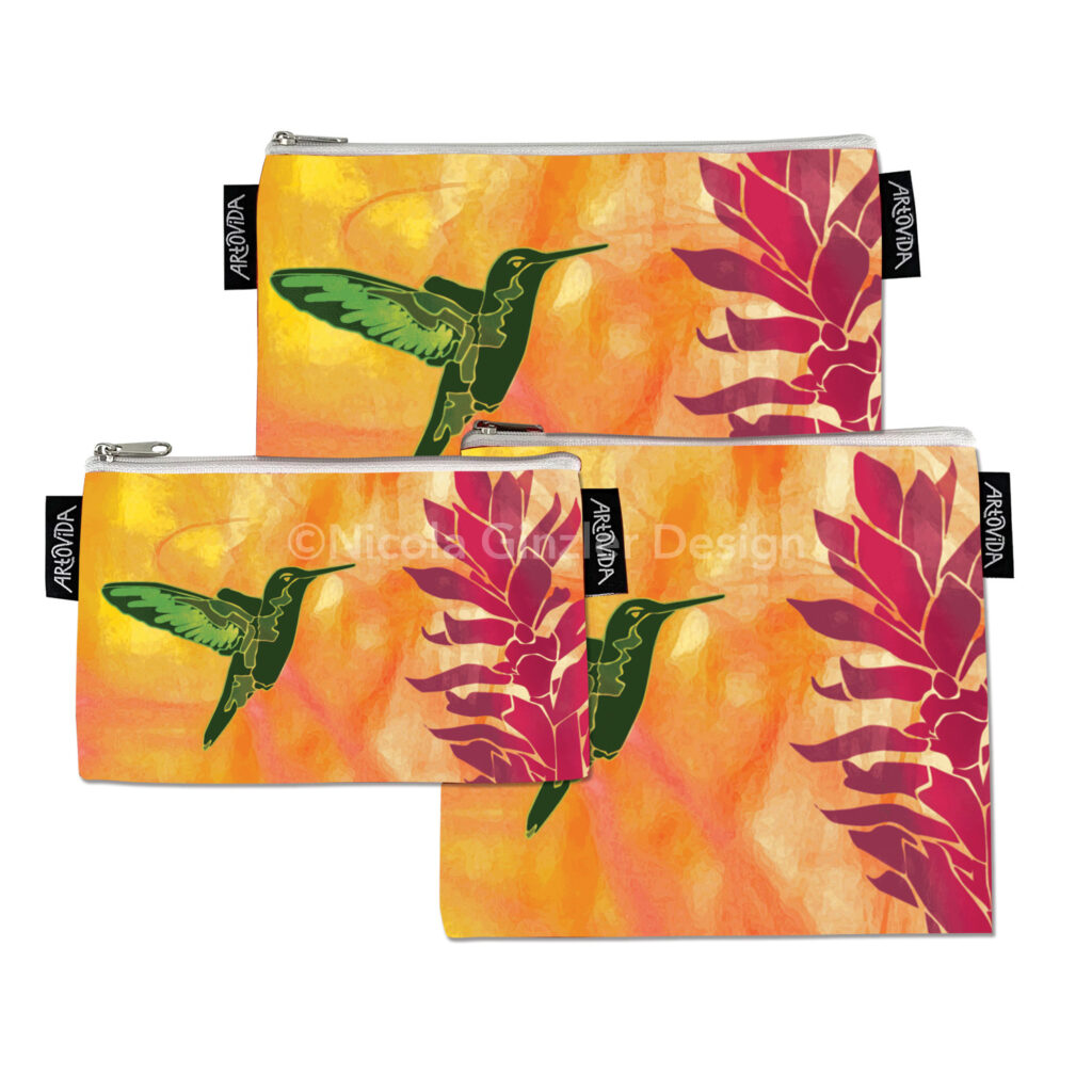 Three zippered pouches of different sizes with hummingbird image on white background. Brightly colored digital illustration of a green hummingbird poised next to a red ginger flower. The background is a vibrant mix of oranges and yellows.
