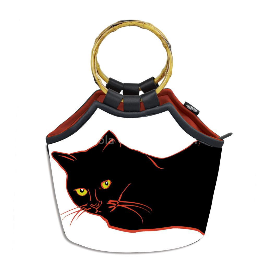 Bag with bamboo handles against white background with cat image. Only head of cat is visible. Cut paper-style digital illustration of a black cat lying down, looking directly at the viewer. The cat has a jagged red outline, yellow-green eyes, and red whiskers.