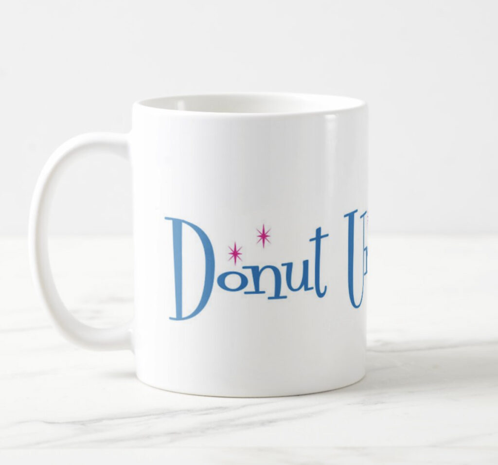 White ceramic mug with Donut Universe logo, left view, on a marble counter.
