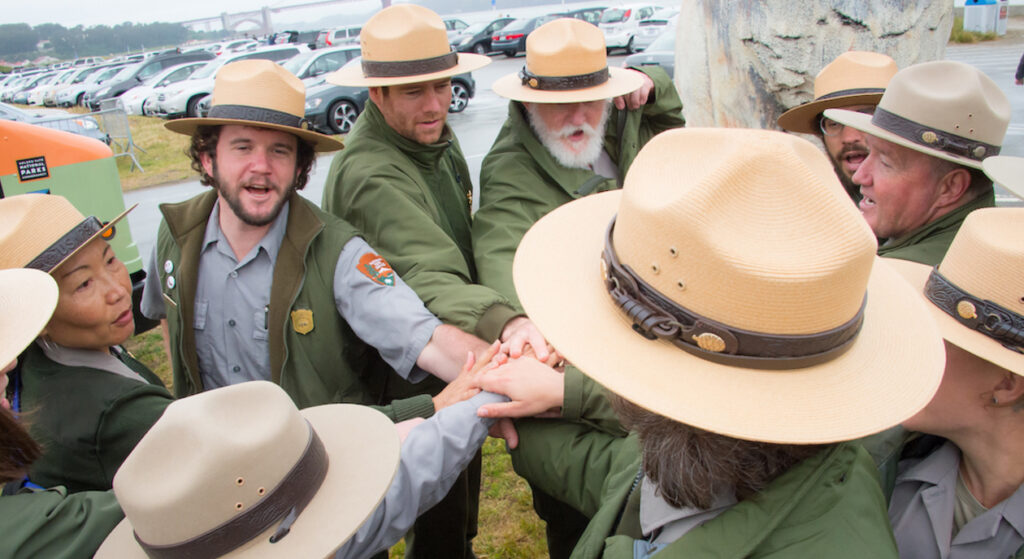 Group of smiling National Parks Service Rangers wearing Ranger clothes and the iconic NPS "flat hats."