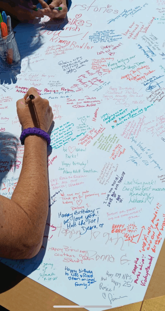 photo of hand signing a big card, with many brightly colored signatures around it.
