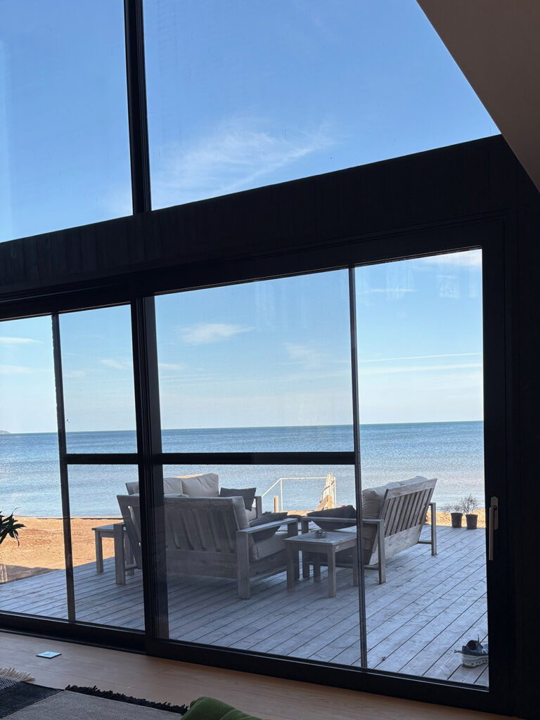 Spare living room with large glass door opening onto wooden deck with view of blue lake