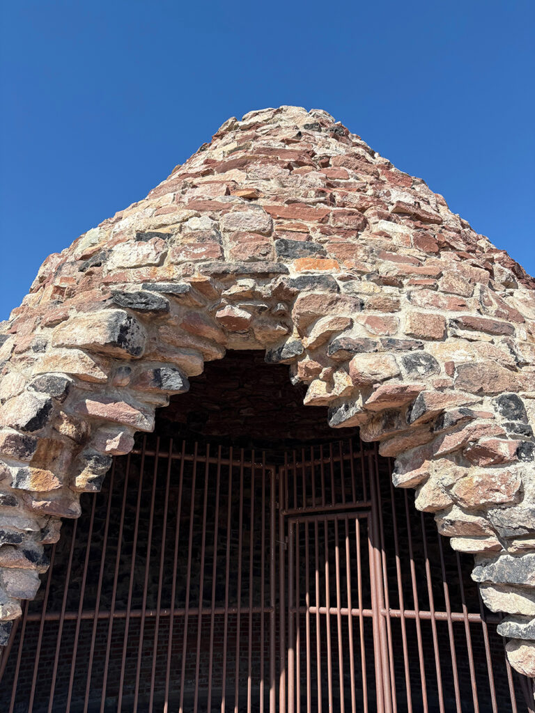 Doorway of beehive-shaped structure with iron grate preventing entry against blue sky