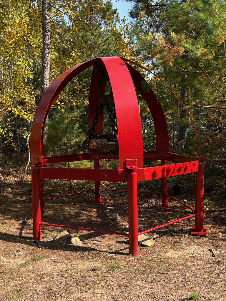 Huge rock hanging from chains on red-painted sculpture