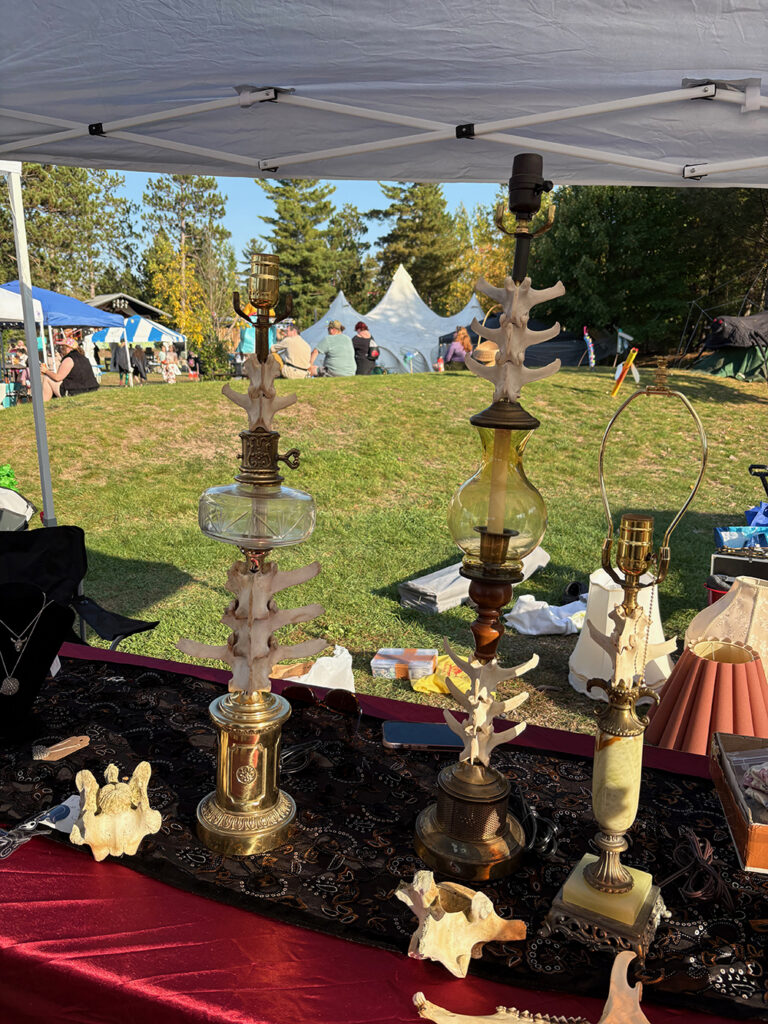 Lamps on table under tent in open field. Upright shafts of lamps have deer vertebrae threaded onto them.