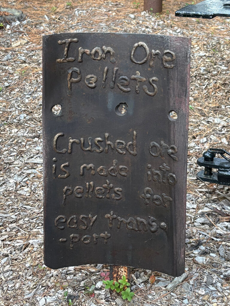 Upright sheet of metal with welds spelling out "Iron Ore Pellets - Crushed or is made into pellets for easy transport"