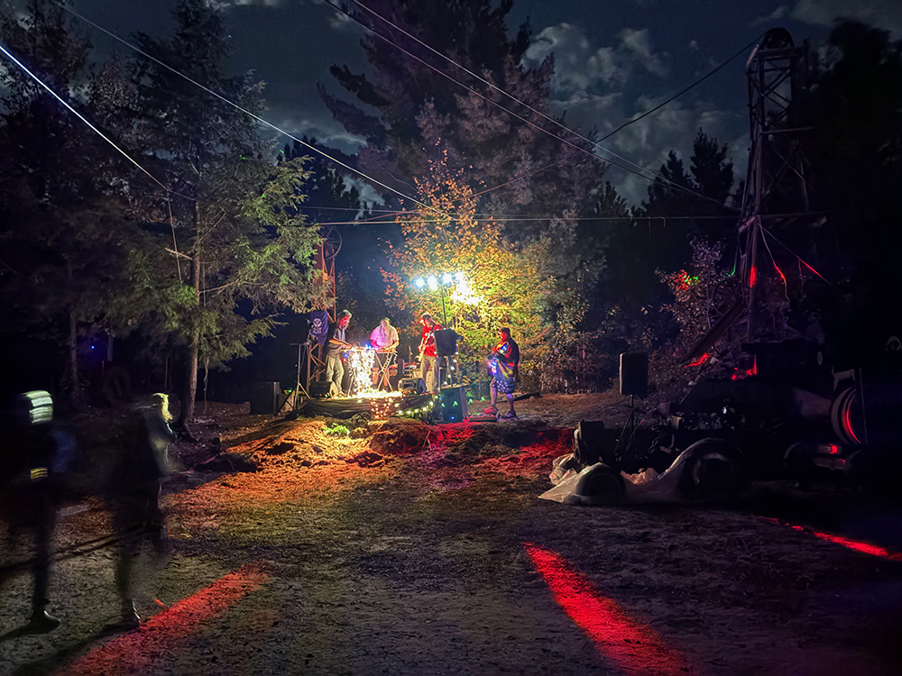 Dark clearing with musicians and bright colored lights