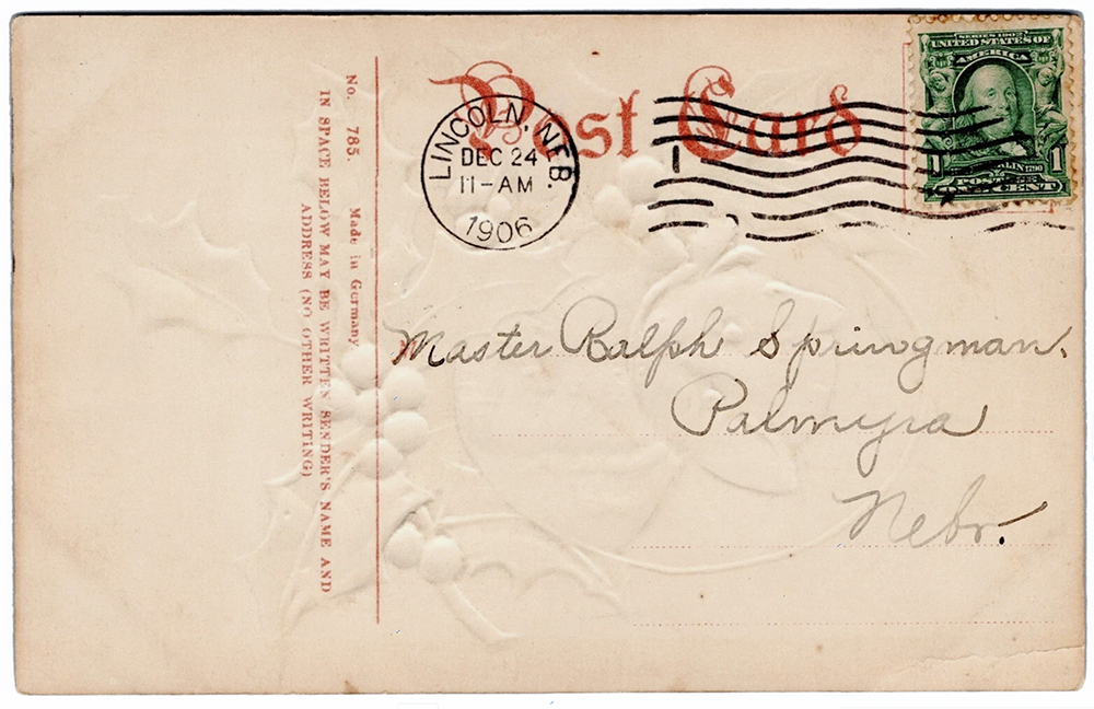 Postcard is addressed in faded black ink to "Master Ralph Springman, Palmyra, Nebr." and postmarked "Lincoln, Nebr., Dec. 24, 1906, 11 - AM." A green 1-cent stamp is cancelled with wavy black lines over red type that says "Post Card." There's a vertical red line to the left of the address, and rotated 90º clockwise below it is red type: "No. 785 - Made in Germany - IN SPACE BELOW MAY BE WRITTEN SENDER'S NAME AND ADDRESS (NO OTHER WRITING)."